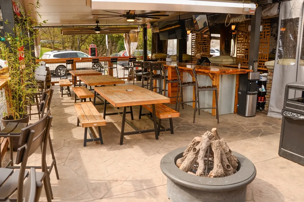 Empty outdoor restaurant patio with fire pit, picnic tables, bar.