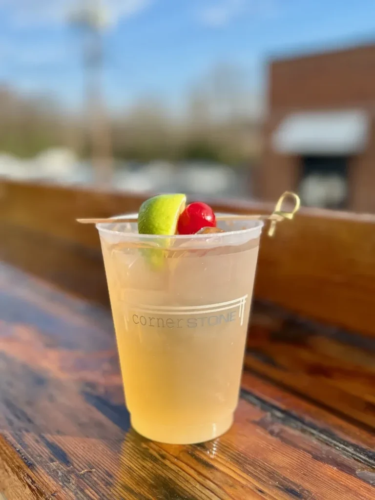 Plastic "cornerSTONE" drink with lime, cherry, ice on wood.
