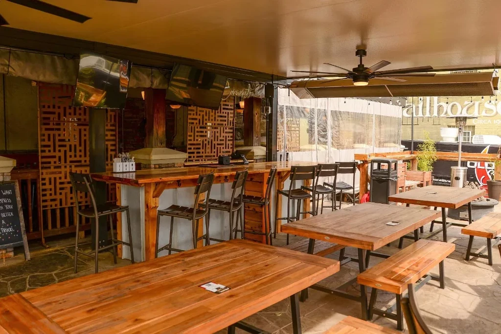 Outdoor rustic restaurant patio with wooden picnic tables, bar, and tent.