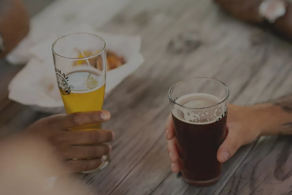 Two hands, different skin tones, hold light and dark beers.