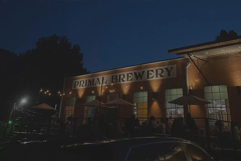 Primal Brewery exterior at night, lit patio with people.