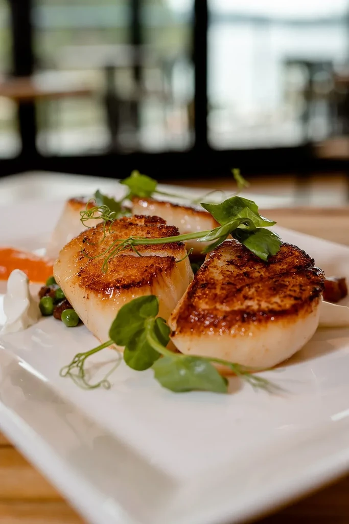 Close-up: Three seared scallops, pea shoots, green peas, and sauces.