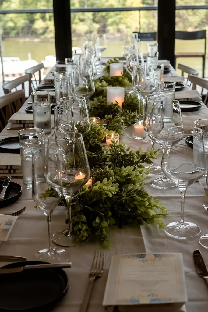 Long dining table with candlelit garland and scenic outdoor view.