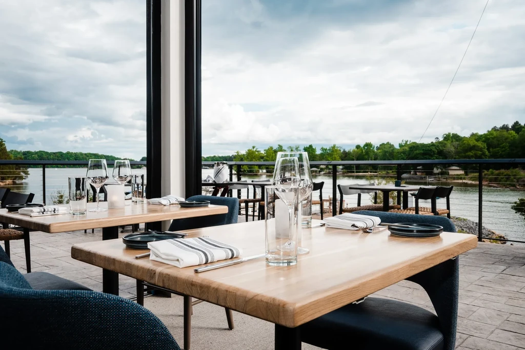 Empty outdoor restaurant patio with set tables overlooking a lake.