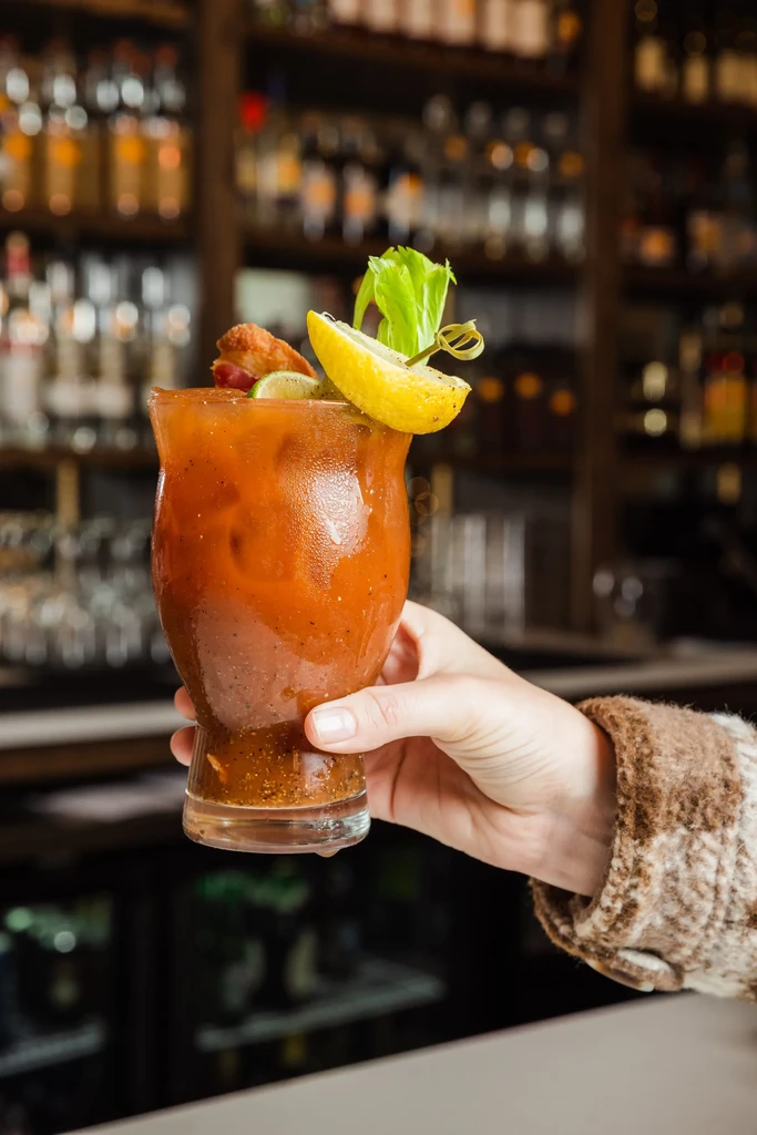 Bloody Mary with celery, citrus, and bacon skewer, held by a hand.