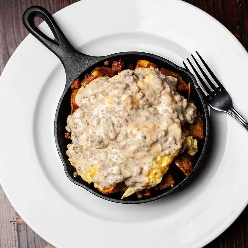 Black skillet filled with crispy potatoes, scrambled eggs, and sausage gravy.