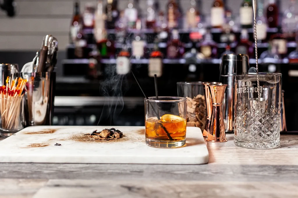 Close-up: amber smoking cocktail with wood smoke on a bar.