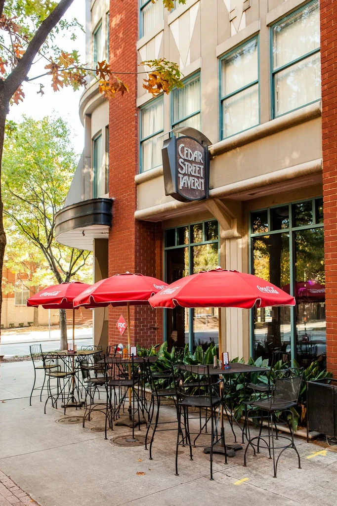 Outdoor patio of Cedar Street Tavern with red Coca-Cola umbrellas and tables.