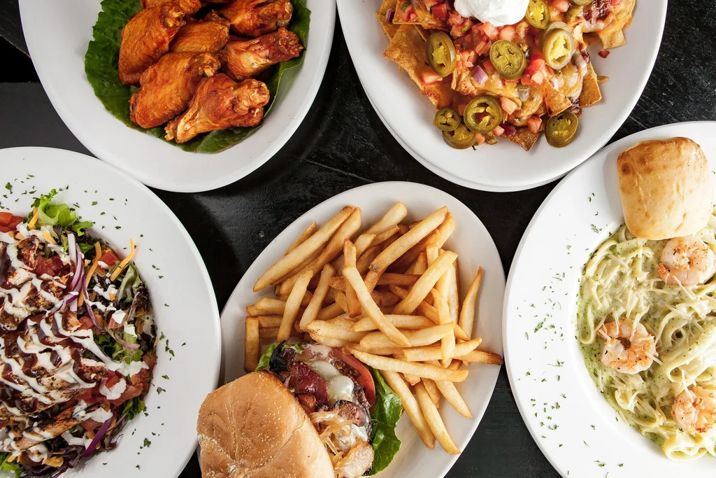Overhead view of five dishes: chicken wings, nachos, pasta, burger, salad.