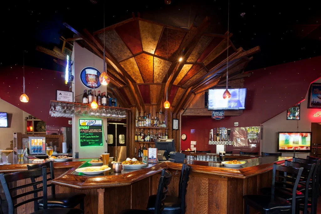 Modern rustic U-shaped bar with food, drinks, and warm lighting.