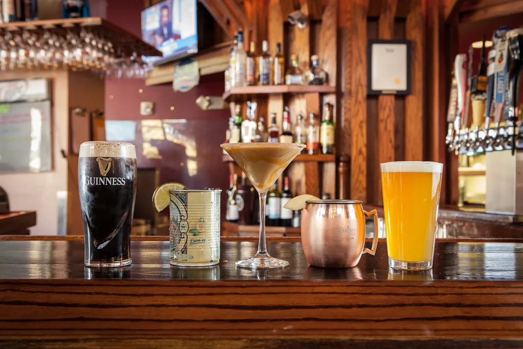 Row of five diverse alcoholic drinks on a dark wooden bar.
