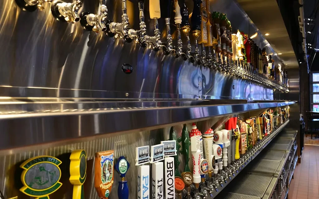 Extensive array of diverse beer taps on a stainless steel bar.