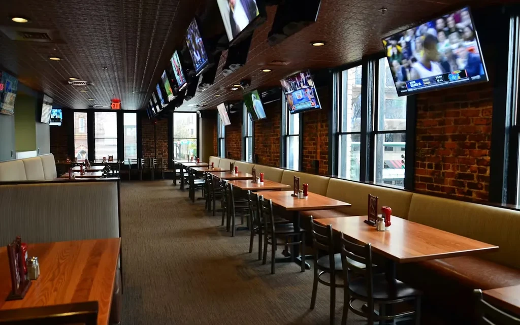 Empty sports bar dining area with booths, brick wall, and many TVs.