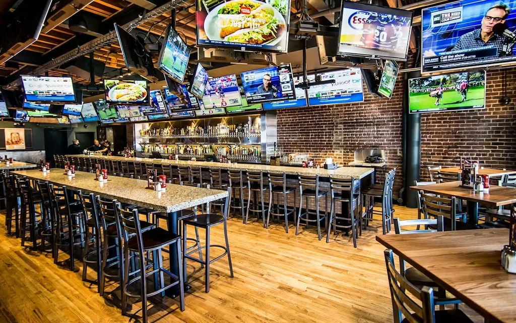 Sports bar interior: numerous TVs, a long bar, and bar stools.
