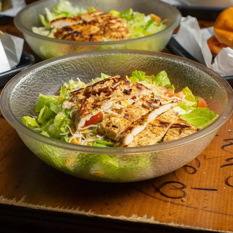 Grilled chicken salads with char marks in glass bowls on wood.