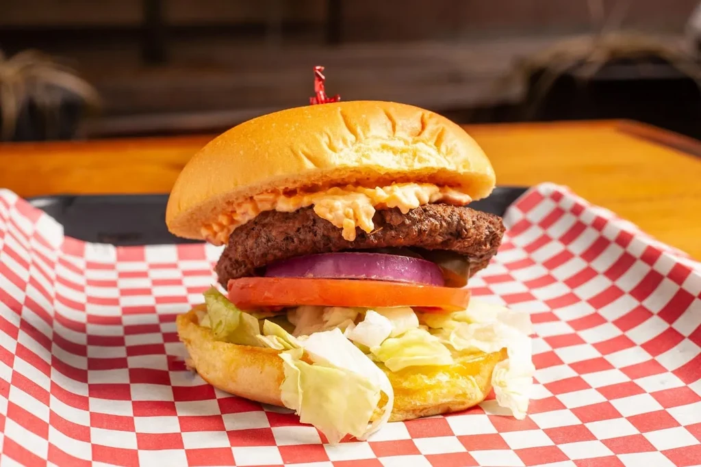 Beef burger in basket with purple onion, creamy sauce, lettuce, tomato.
