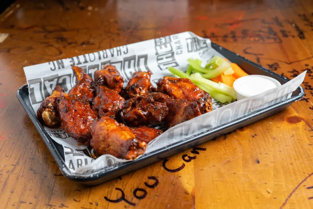 Black tray with saucy chicken wings, celery, carrots, and dip.