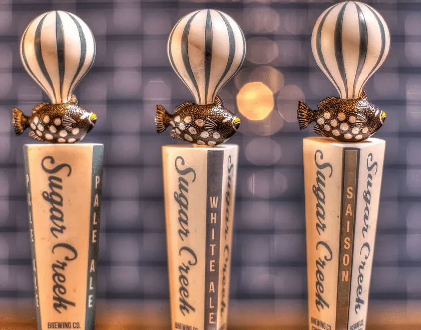 Three Sugar Creek beer taps with ornate fish and balloon toppers.