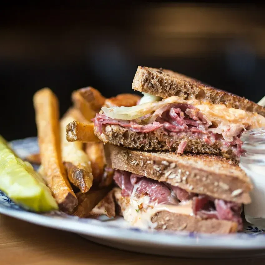 Reuben sandwich, golden fries, and a pickle spear on a patterned plate.