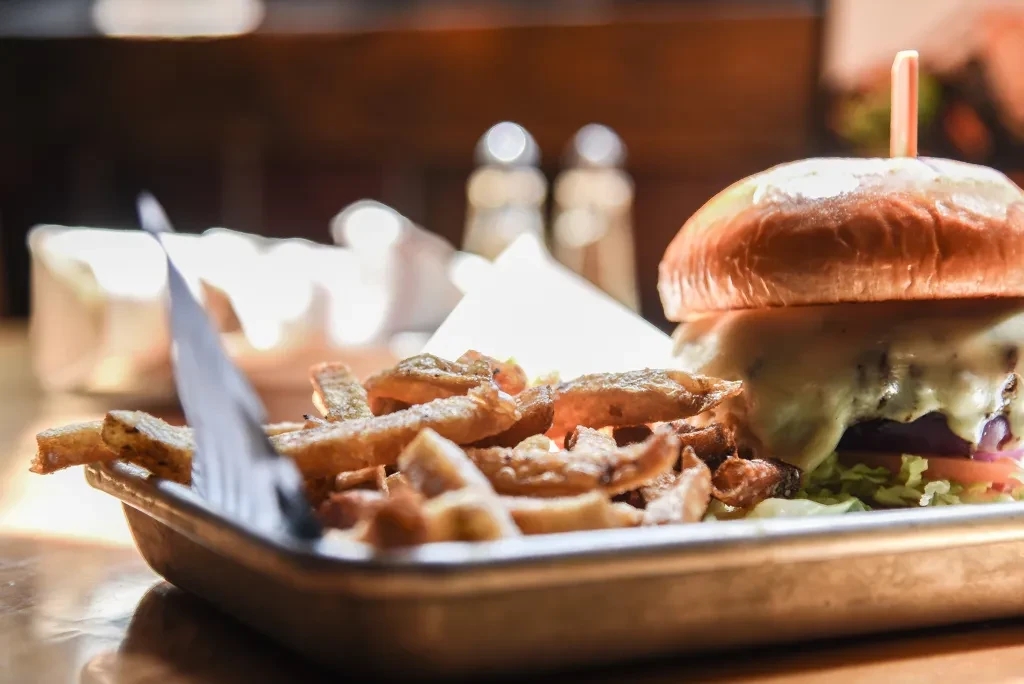 Gourmet burger with melted cheese and french fries on a metal tray.