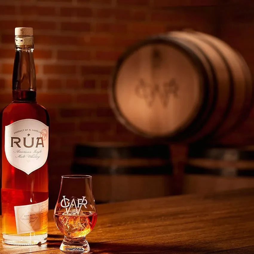 RÚA American Single Malt Whiskey bottle, glass with ice, wood and brick.