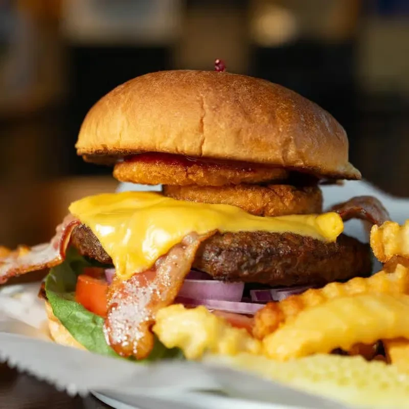 Loaded burger with bacon, melted cheese, onion rings, and waffle fries.