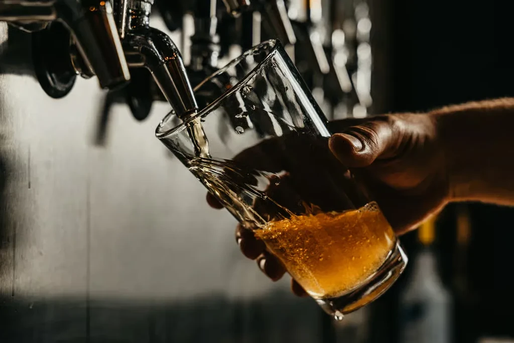 Hand holding glass as foamy golden beer pours from a tap.