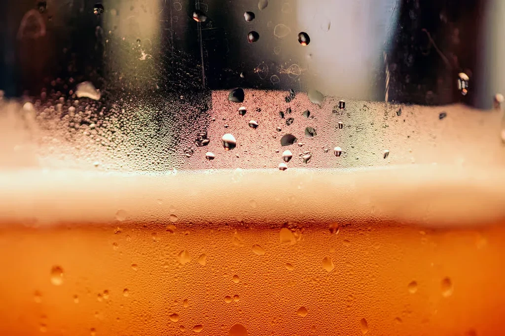 Macro shot of a cold glass with amber liquid and condensation.