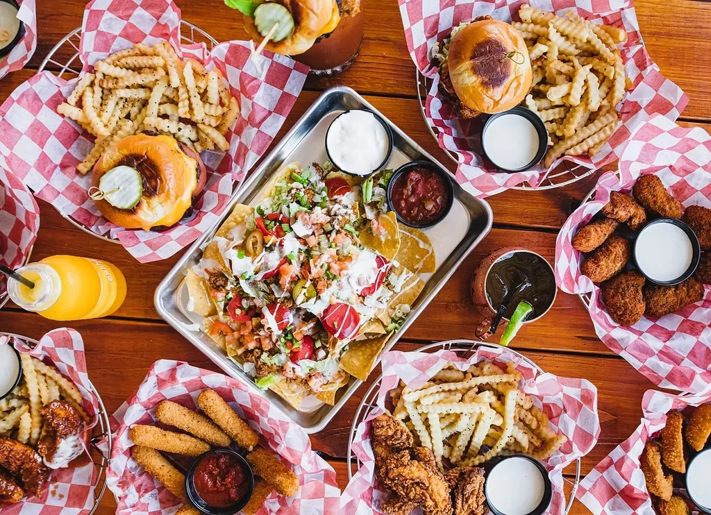 Table laden with cheeseburgers, fries, nachos, chicken tenders, and beverages.