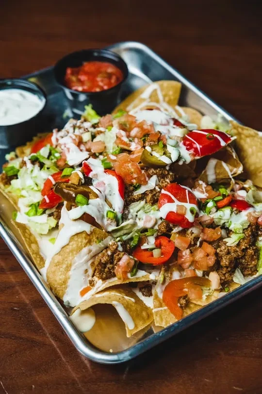 Close-up of loaded nachos with meat, vegetables, sour cream, and salsa.