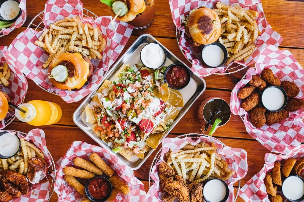 Overhead view: restaurant table with burgers, fries, wings, nachos, drinks.