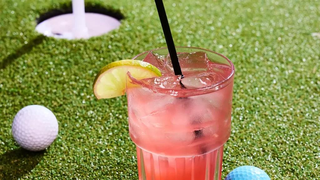 Pink drink with lime and ice on a golf putting green.