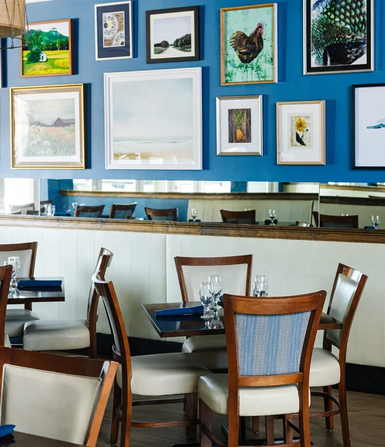 Restaurant interior with vibrant blue wall, framed art, and empty tables.