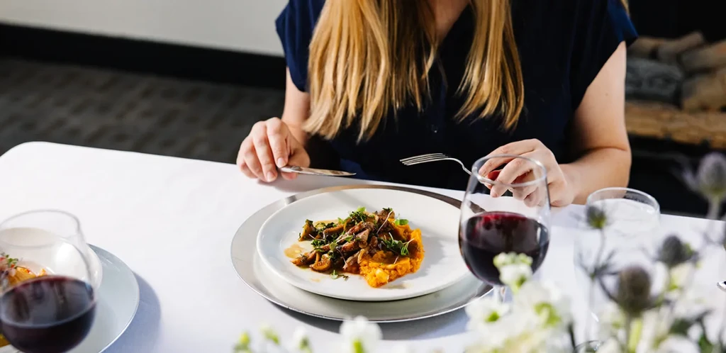 Plated sweet potato/squash, mushrooms, red wine, person about to eat.