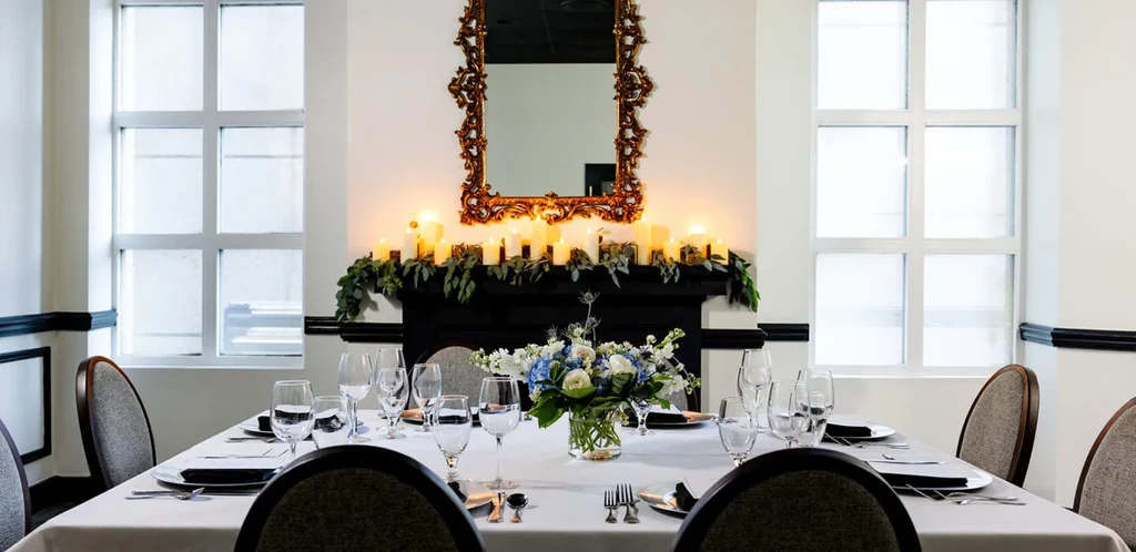 A long dining table set with plates, flowers, candles, and a fireplace.