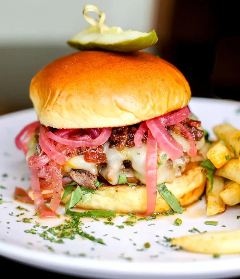Gourmet burger with melted cheese, bacon jam, pickled red onions, and fries.