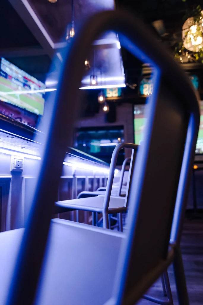Modern bar interior with blue and purple lighting, bar stools, sports screens.