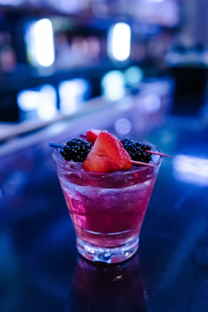 Iced pink cocktail garnished with blackberries and a strawberry.