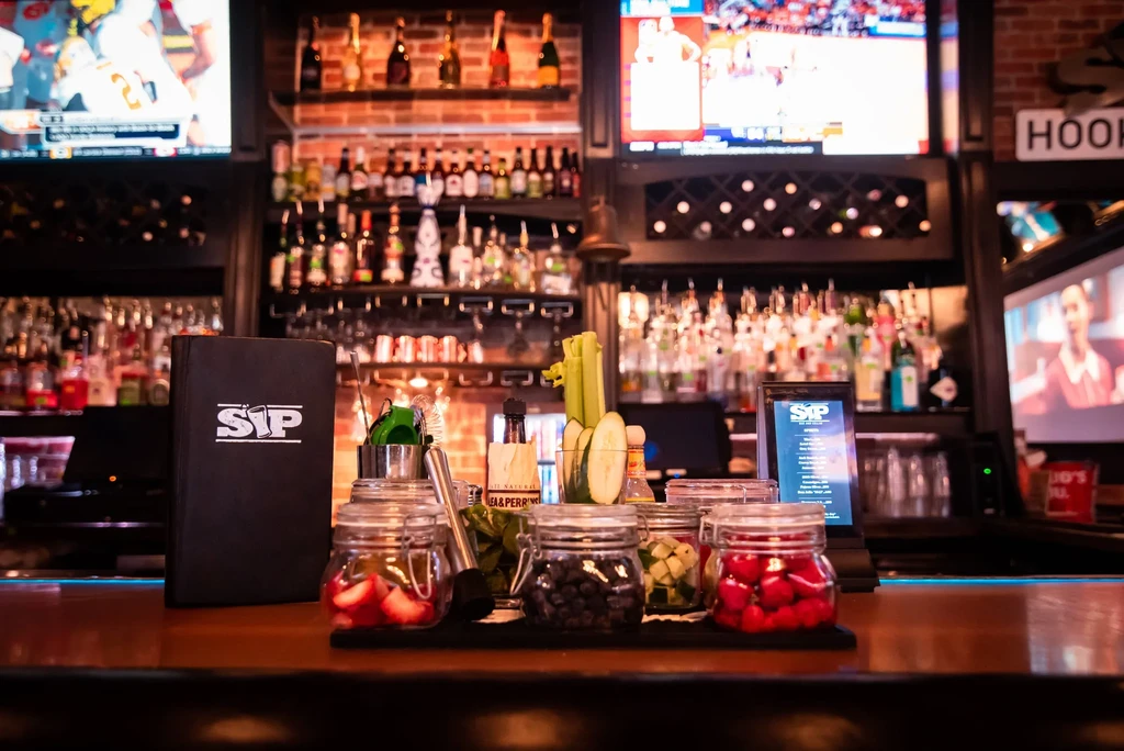 Modern gastropub bar counter with fresh cocktail ingredients and sports TVs.