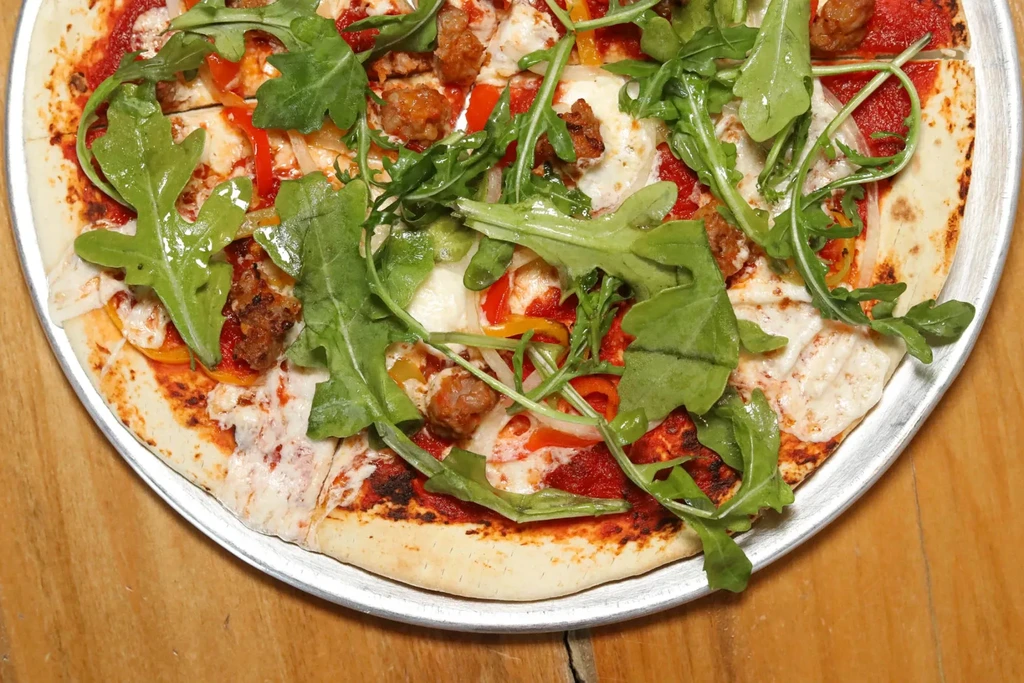 Overhead view: pizza with sausage, peppers, mozzarella, and arugula.