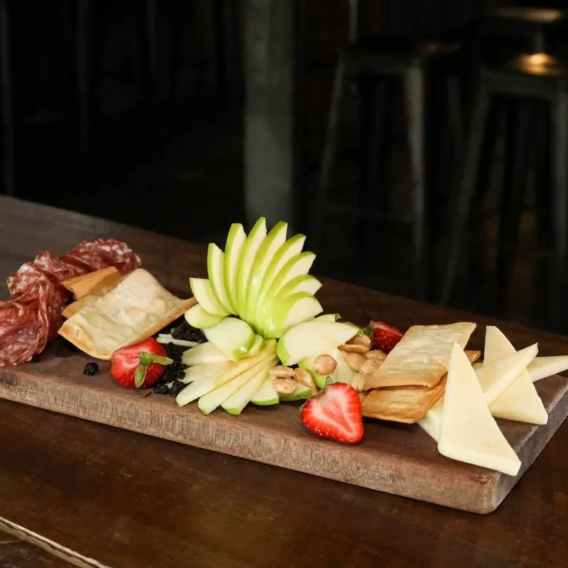 Rustic wooden charcuterie board with salami, cheese, fruit, crackers.