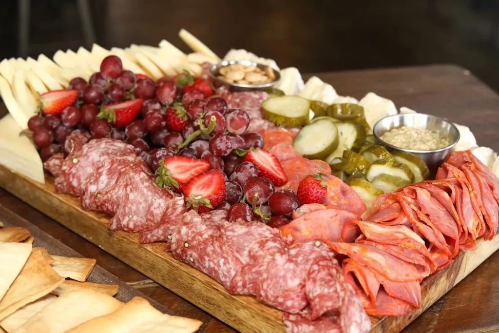 Charcuterie board with cheese, grapes, cured meats, pickles, and condiment.