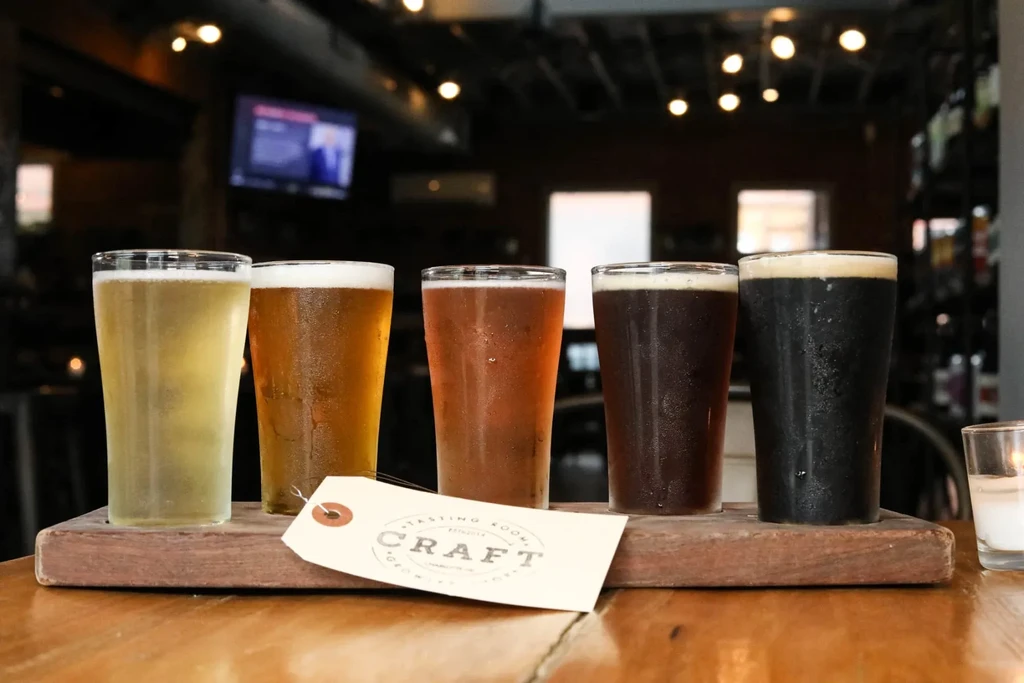 Five cold craft beers on a rustic wooden paddle, lightest to darkest.