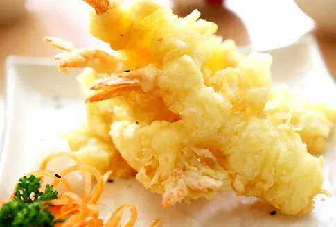 Crispy golden shrimp tempura stacked on a white plate with green garnish.