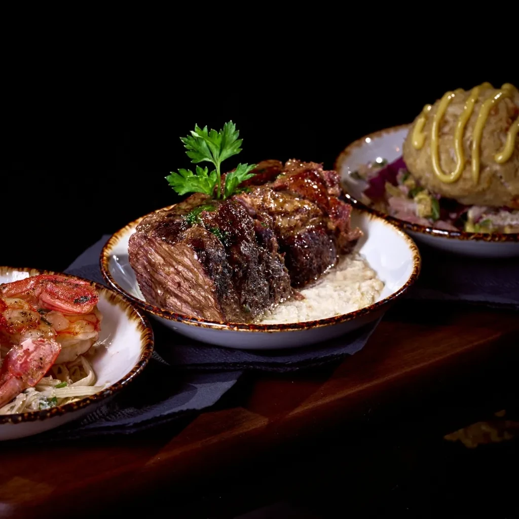 Close-up of three restaurant dishes: braised meat, shrimp, potato ball.