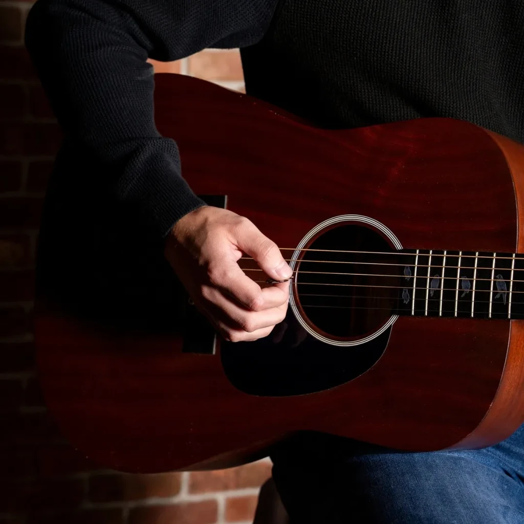 Close-up of person strumming acoustic guitar with bird fretboard inlays.