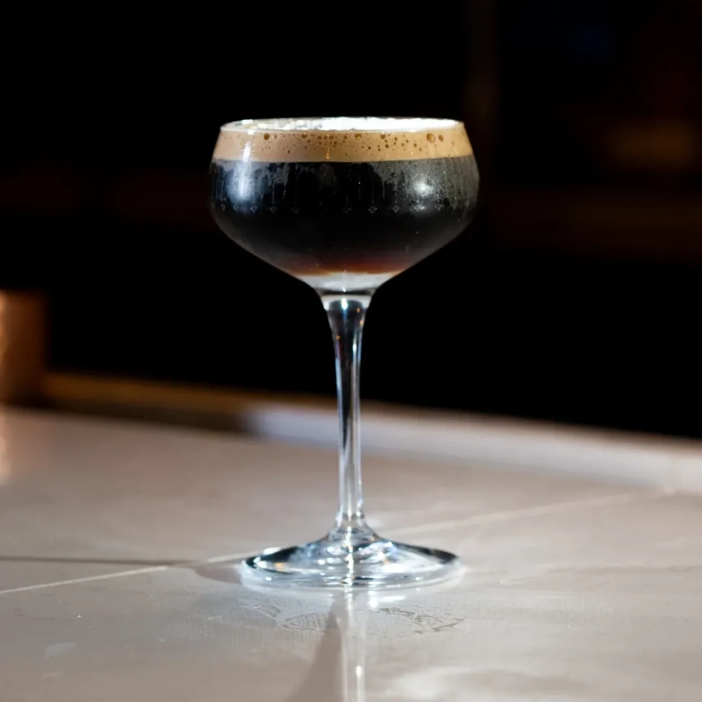 Frothy dark cocktail in a stemmed coupe glass on stone.