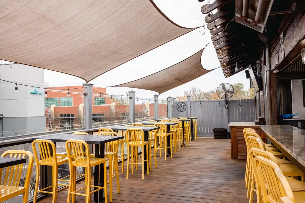 Urban patio with yellow bar stools, black tables, and shade sails.
