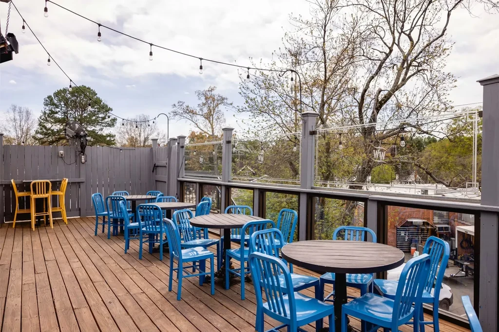 Outdoor wooden patio with blue chairs, yellow stools, and string lights.