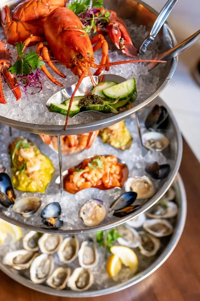 Multi-tiered seafood tower with lobster, oysters, and various seafood on ice.